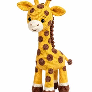 Op de afbeelding: Een gehaakte giraf knuffel met een geel lichaam, bruine vlekken, een cr&egrave;mekleurige snuit en donkerbruine hoeven. Het speelgoed heeft twee kleine hoorntjes op de kop, grote zwarte veiligheidsogen en een donkerbruine manen langs de nek.