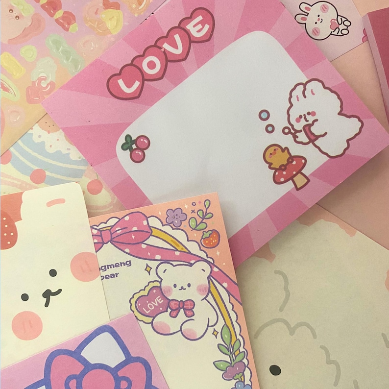 May include: A collection of pink and pastel-colored sticky notes and stationery. The notes feature cute illustrations of bunnies, bears, and other whimsical designs. One note has the word "LOVE" in a heart-shaped design.