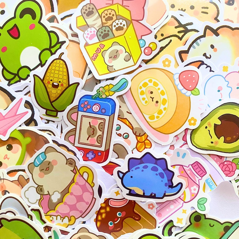 May include: A collection of colorful stickers featuring various cute illustrations. Designs include a green frog, a smiling corn, a bear in a teacup, a blue dinosaur, a roll cake, and a handheld game console. The stickers have a cartoon style.