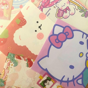 May include: A collection of colorful, patterned stationery featuring cute cartoon characters. Designs include a white bear with a pink bow, a strawberry-themed design, and a Hello Kitty illustration. The stationery is in shades of pink, white, and pastel colors.