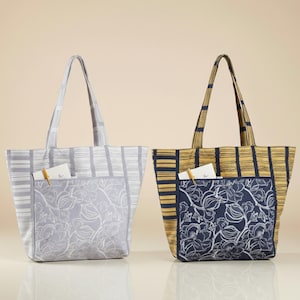 May include: Two tote bags. One is light gray with a floral pocket and striped pattern. The other is navy blue and gold with a floral pocket. Both have handles and a pocket.