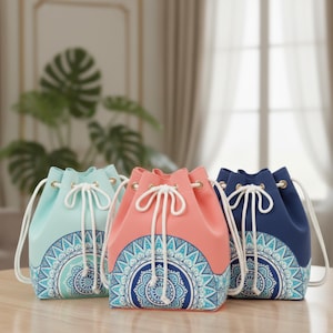 以下が含まれることがあります： パステルカラーの巾着バッグ3つ。ライトブルー、コーラル、ネイビー。各バッグは白い巾着開閉部と、下部に青と白のマンダラ模様が特徴です。明るい色の木製の表面にバッグが展示されています。