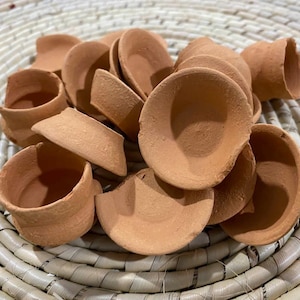 Może przedstawiać: Kolekcja małych, terakotowych glinianych misek i pojemników. Miski mają płytki, zaokrąglony kształt, a pojemniki są cylindryczne. Ułożone są na tkanej, jasnej macie.