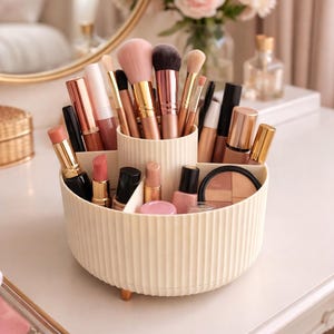 May include: A cream-colored, multi-compartment makeup organizer filled with various cosmetic products and makeup brushes. The organizer sits on a white vanity table, with a mirror and flowers in the background.