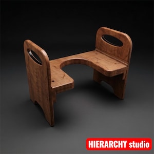 May include: A wooden toilet stool with a natural finish. The stool has a U-shaped cutout in the center and two upright sections with oval-shaped handles. The stool is designed to assist with proper posture during bathroom use. The text "HIERARCHY studio" is in the bottom right corner.