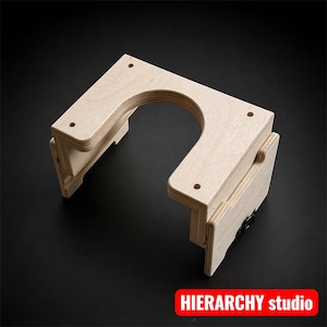 May include: A light-colored wooden structure with a U-shaped cutout and hinged sections. The design features multiple layers of wood and is set against a dark background. The text "HIERARCHY studio" is displayed in a red rectangle.