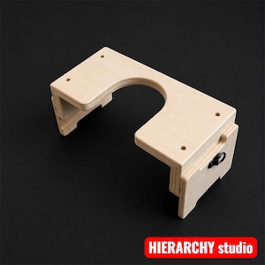 May include: A light-colored wooden desk attachment with a curved cutout and a rectangular shape. It has several drilled holes and a metal ring on the side. The text "HIERARCHY studio" is in a red rectangle.
