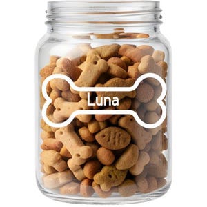 May include: A glass jar filled with dog biscuits. A white bone-shaped label with the name "Luna" is on the front. The biscuits are various shapes and shades of brown.