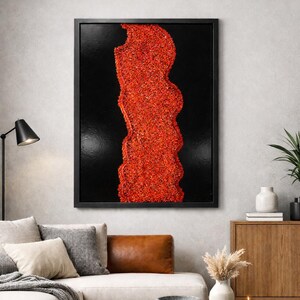 May include: Abstract wall art featuring a textured, vertical design in vibrant red against a black background, framed in a black border. The artwork is displayed in a modern living room setting, above a sofa with neutral-toned cushions.