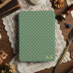 May include: A green notebook with a white polka dot pattern and gold initials. The notebook is on a wooden surface with a pocket watch, owl figurine, and other vintage items.