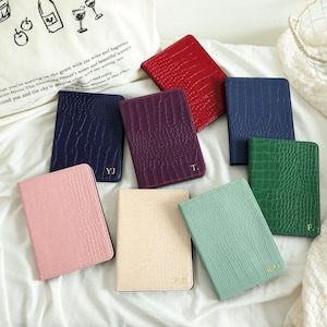 Peut inclure: Un ensemble de huit porte-passeports rectangulaires présentant un motif texturé en peau de crocodile dans diverses couleurs, dont rouge, bleu marine, violet, rose, crème, vert menthe, vert foncé et bleu, avec des initiales dorées embossées.