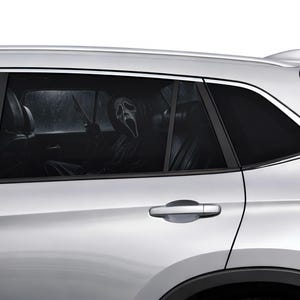 May include: A silver SUV with tinted windows. Inside, a person in a Scream mask and black robe holds a knife. The interior is dark, contrasting with the bright exterior. A Halloween-themed image.