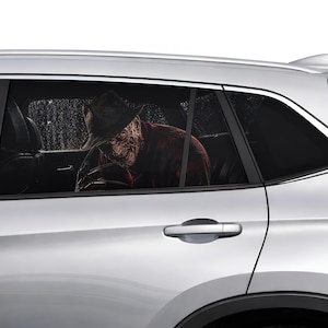 Pode incluir: Um carro prateado com vidros fumados. No interior, uma figura semelhante a Freddy Krueger é visível, usando um chapéu e uma camisa xadrez vermelha e preta. A cena sugere um tema de terror.