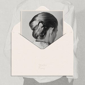 Può includere: Immagine in bianco e nero di un'acconciatura femminile a chignon, fissata con una clip e un pettine neri, presentata in una busta color crema. Il testo include "Studio Remy" e frasi sulla moda e il design.