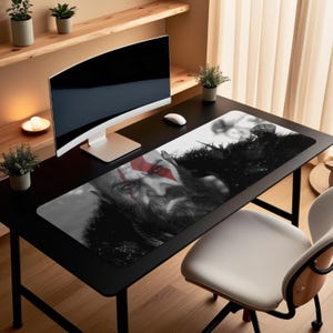 Puede incluir: Alfombrilla de ratón rectangular en blanco y negro con la imagen de un personaje barbudo con marcas rojas en la cara. La alfombrilla está sobre un escritorio negro, con un monitor de ordenador y un ratón.