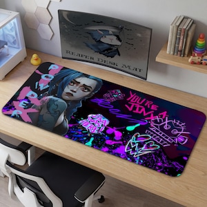 May include: A rectangular desk mat with a vibrant design. It features a character with blue hair and tattoos, alongside the text "POWER" and "YOU'RE JINX". The mat has a black background with neon pink and purple splashes.