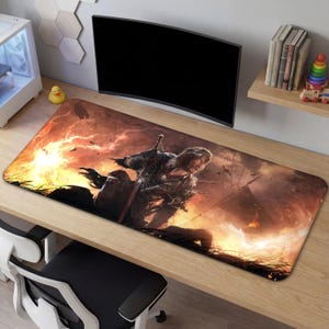 May include: A rectangular gaming mouse pad featuring a warrior in a fiery battle scene. The pad has a black border and a detailed illustration with shades of orange, red, and brown. The design includes a sword and a dramatic, action-packed environment.