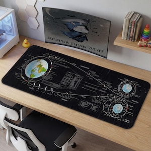Può includere: Tappetino da scrivania nero con un diagramma dettagliato della Terra e di altri corpi celesti. Il tappetino presenta linee e testo bianchi, con una grafica colorata della Terra. Il testo "REAPER DESK MAT" è visibile sul monitor sullo sfondo.