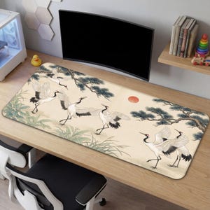May include: A rectangular desk mat with a Japanese-inspired design. It depicts white cranes, a red sun, and pine trees on a beige backdrop. The mat is positioned on a wooden desk, suitable for a computer setup.