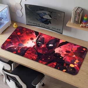 May include: A rectangular desk mat featuring a vibrant illustration of Deadpool in his signature red and black suit. The background is a dynamic mix of red hues and abstract shapes. The mat is designed for computer use.