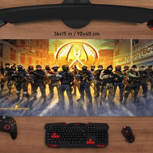 May include: A large rectangular gaming mouse mat with a Counter-Strike design, depicting a team of soldiers against a city backdrop. The mat measures 90x40 cm. A black keyboard, mouse, and controller are also visible.