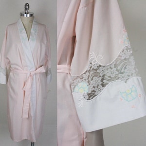 May include: A pink satin robe with white lace trim and floral embroidery. The robe has a shawl collar, long sleeves, and a tie belt.