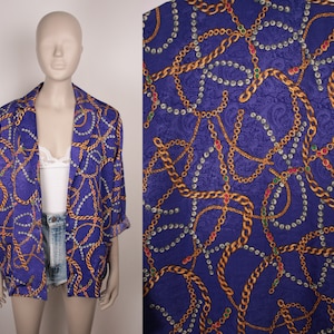 May include: A purple satin blazer with a gold chain and pearl necklace print. The blazer has a long sleeve and a relaxed fit.