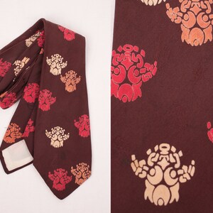 May include: A brown silk tie with a repeating pattern of stylized floral designs in shades of red, orange, and cream.