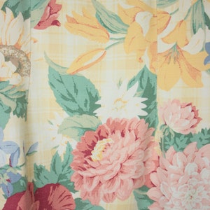 May include: A yellow fabric with a floral pattern. The pattern features pink, red, white, and yellow flowers with green leaves. The fabric has a checkered pattern.