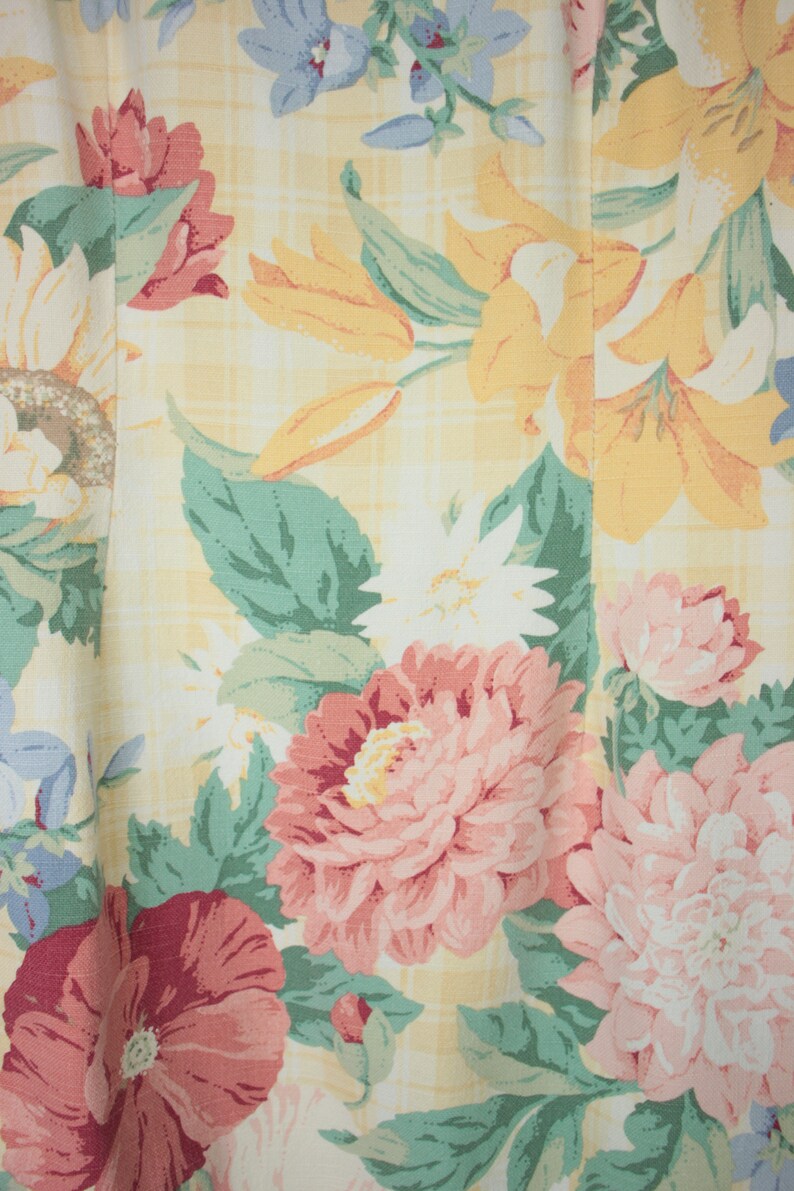 May include: A yellow fabric with a floral pattern. The pattern features pink, red, white, and yellow flowers with green leaves. The fabric has a checkered pattern.