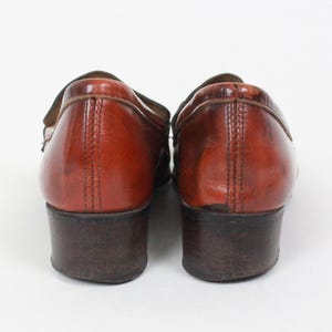 May include: A pair of brown leather loafers with a low heel. The shoes have a slightly distressed look and are made of a soft, supple leather.