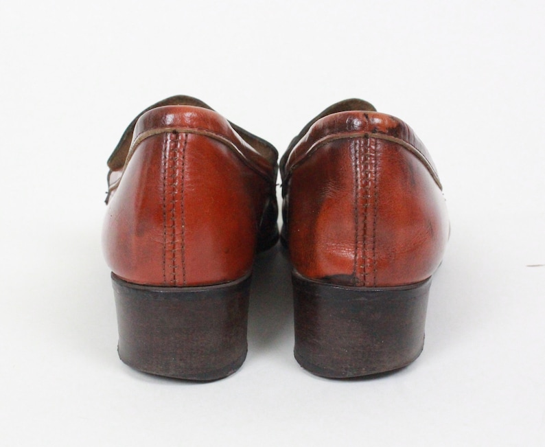 May include: A pair of brown leather loafers with a low heel. The shoes have a slightly distressed look and are made of a soft, supple leather.