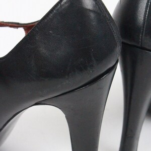 May include: Black leather high-heeled shoes. The shoes have a classic design with a rounded toe and a slender heel. The heels are approximately 3 inches tall. The shoes appear to be vintage.