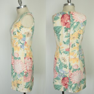 May include: A sleeveless dress with a floral print featuring sunflowers, pink and red flowers, and green leaves on a yellow background. The dress has a back zipper closure.