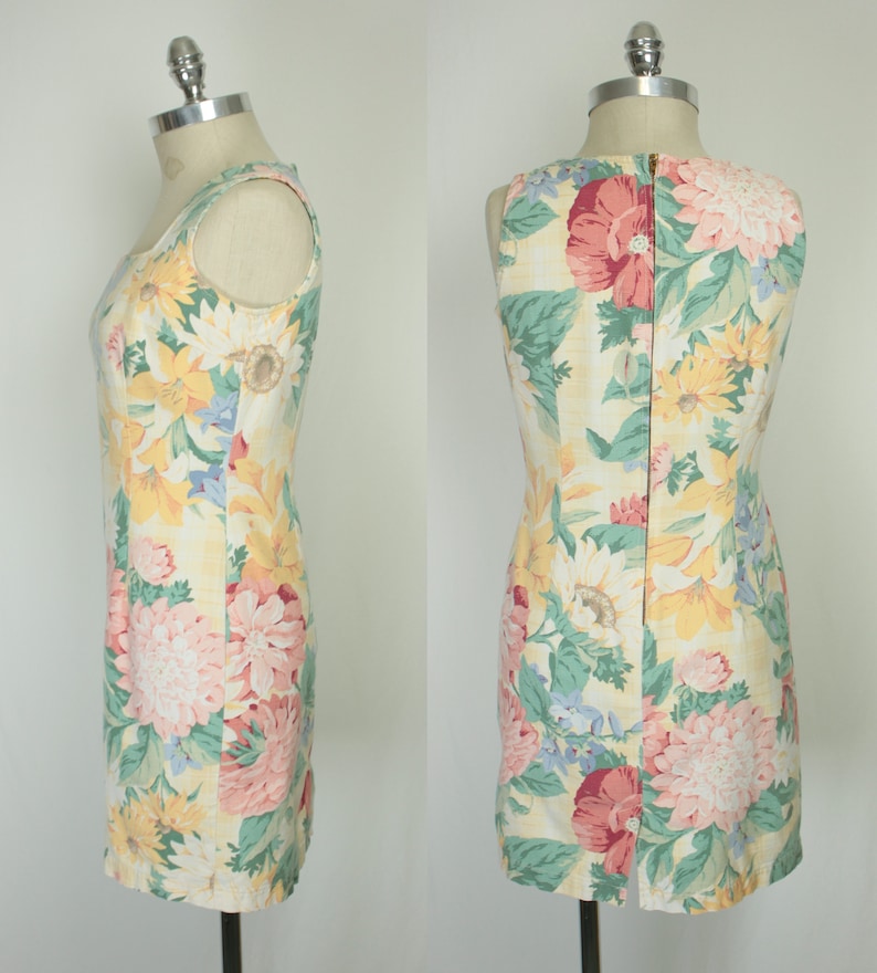 May include: A sleeveless dress with a floral print featuring sunflowers, pink and red flowers, and green leaves on a yellow background. The dress has a back zipper closure.
