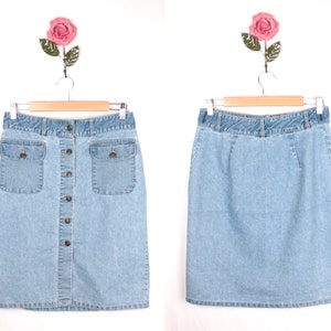 May include: A light blue denim skirt with a button front closure and two front pockets. The skirt is hanging on a wooden hanger.