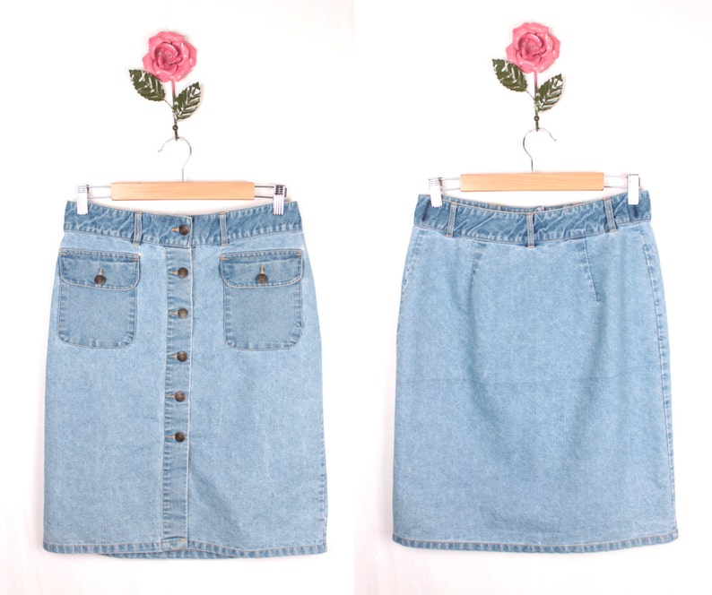 May include: A light blue denim skirt with a button front closure and two front pockets. The skirt is hanging on a wooden hanger.