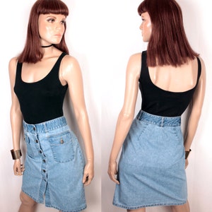 May include: A light blue denim skirt with a button front closure and a single pocket on the right side. The skirt is paired with a black tank top.