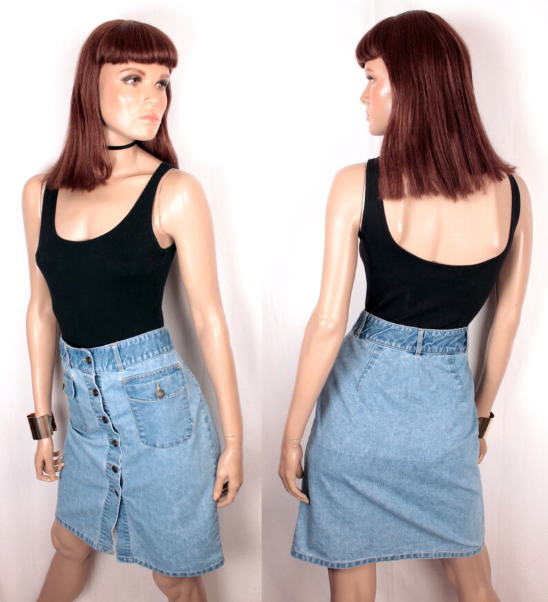 May include: A light blue denim skirt with a button front closure and a single pocket on the right side. The skirt is paired with a black tank top.