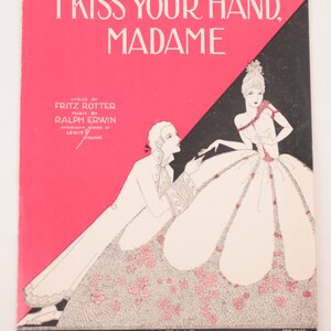 May include: A vintage sheet music cover with a pink and black background. The cover features a black and white illustration of a man and woman in a romantic setting. The title of the song is "I Kiss Your Hand, Madame".
