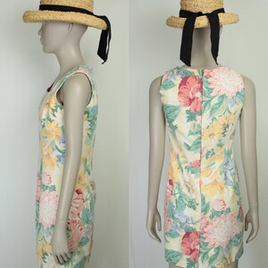 May include: A sleeveless floral print dress with a yellow, pink, green, and blue color scheme. The dress has a zipper closure in the back and is paired with a straw hat with a black ribbon.