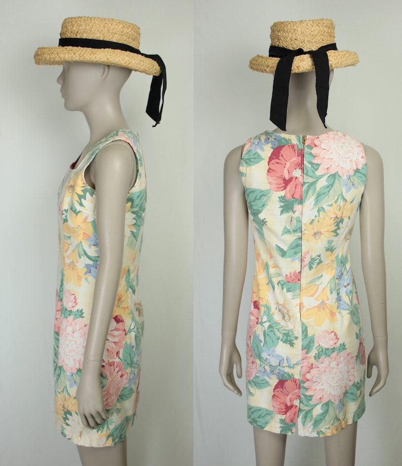 May include: A sleeveless floral print dress with a yellow, pink, green, and blue color scheme. The dress has a zipper closure in the back and is paired with a straw hat with a black ribbon.