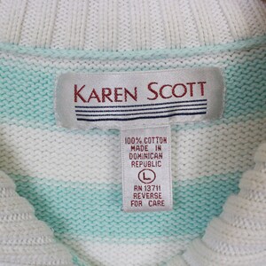 Op de afbeelding: Een wit en lichtblauwe gestreepte trui met een wit label waarop "KAREN SCOTT" en "100% KATOEN GEMAAKT IN DOMINICAANSE REPUBLIEK L RN 13711 ACHTERZIJDE VOOR ZORG" staat.