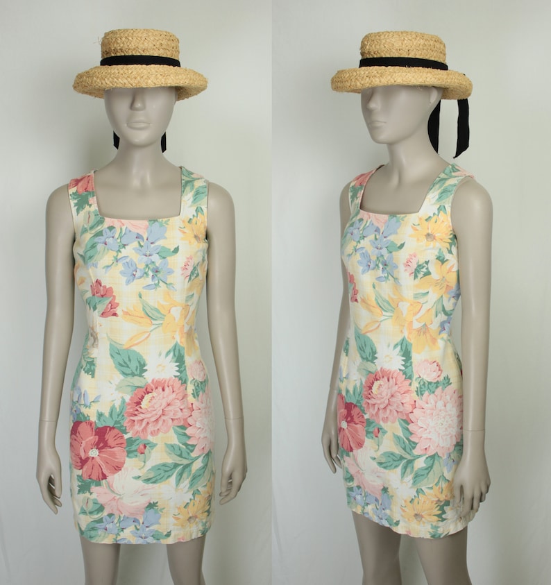 May include: A sleeveless, yellow floral print dress with a square neckline. The dress is fitted and has a short length. The model is wearing a straw hat with a black ribbon.