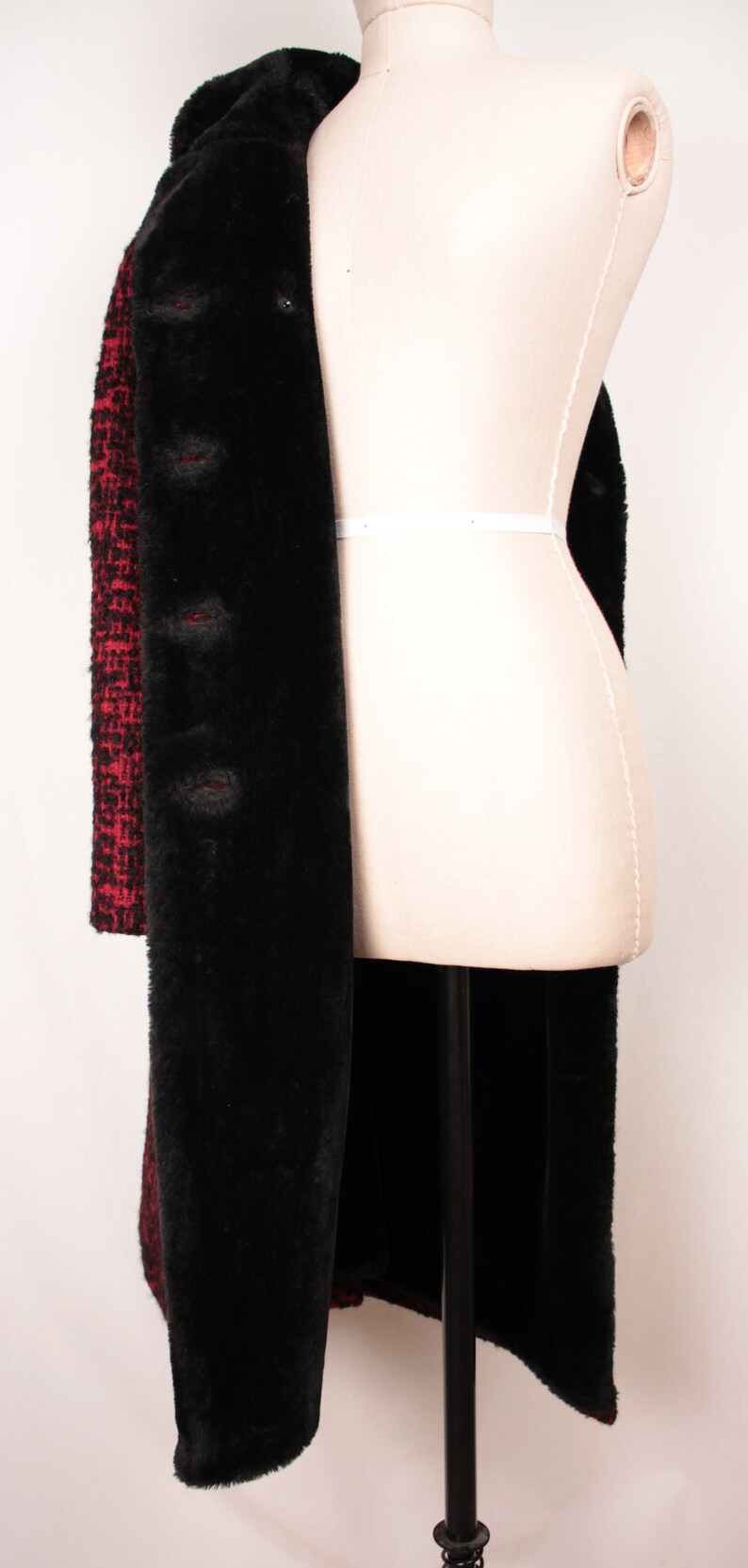 May include: A long black and red coat with a faux fur lining. The coat is on a white dress form.