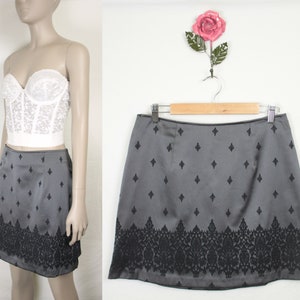 May include: A gray mini skirt with a black floral pattern around the bottom hem and a black diamond pattern throughout the skirt.