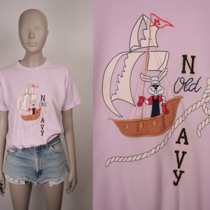 May include: Pink t-shirt with a white embroidered sailboat, a rabbit wearing a red and blue outfit, and the text "N Old Navy".