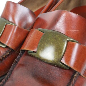 May include: A pair of brown leather loafers with a buckle closure. The loafers have a pointed toe and a low heel.
