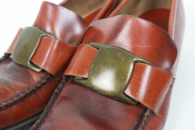 May include: A pair of brown leather loafers with a buckle closure. The loafers have a pointed toe and a low heel.