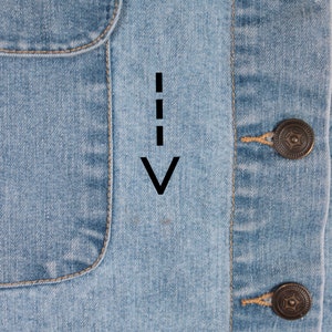 May include: Close-up of a light blue denim jacket with a pocket on the left side and a button closure on the right side. The jacket has a light brown stitching detail.